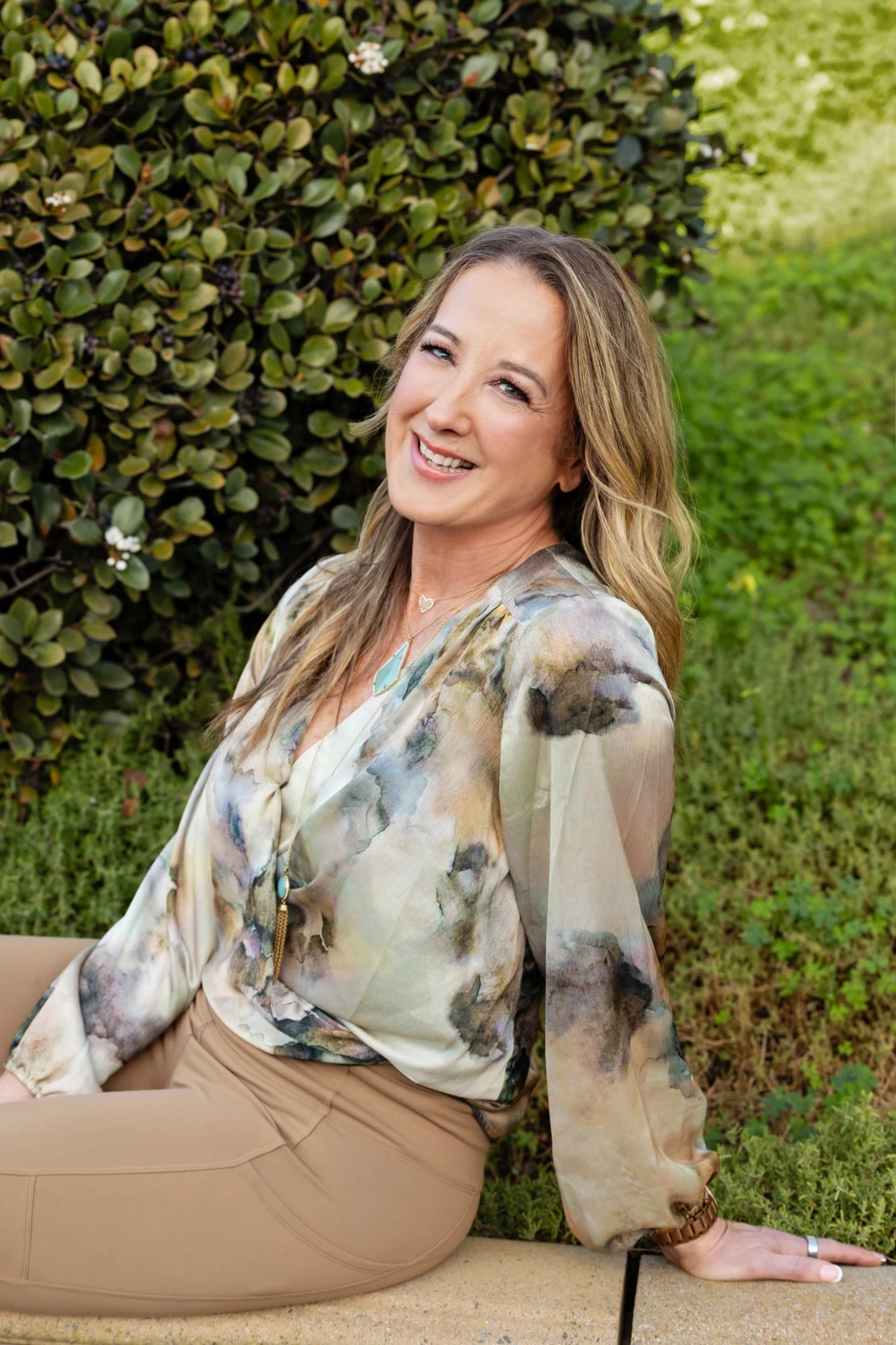 RoxAnne Eli seated outdoors beside a green hedge